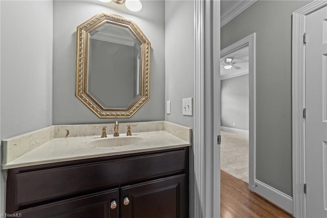 bathroom featuring baseboards, wood finished floors, vanity, and crown molding