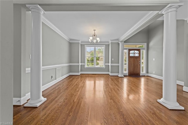 foyer featuring a notable chandelier, ornamental molding, wood finished floors, and ornate columns