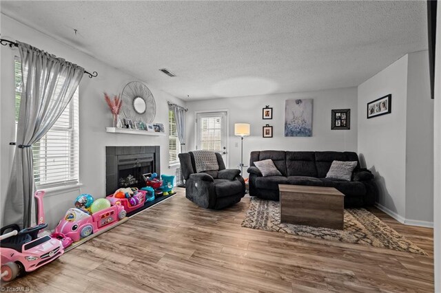 living room featuring a tiled fireplace, a wealth of natural light, a textured ceiling, and hardwood / wood-style flooring