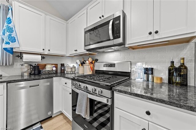 kitchen featuring white cabinets, light hardwood / wood-style flooring, backsplash, appliances with stainless steel finishes, and dark stone countertops