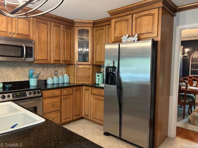 kitchen with brown cabinets, light tile patterned flooring, a notable chandelier, stainless steel appliances, and backsplash