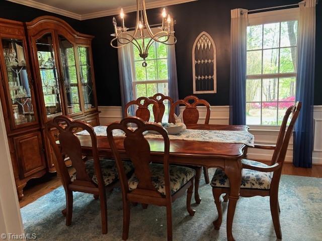 dining room featuring crown molding, a notable chandelier, wood finished floors, and a decorative wall