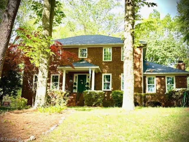 colonial house with brick siding, a chimney, and a front yard