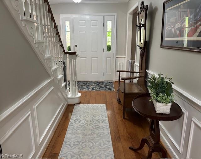 entryway featuring crown molding, wood finished floors, stairway, and a decorative wall