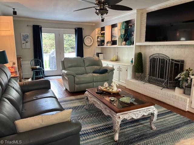 living area with ornamental molding, a brick fireplace, ceiling fan, and wood finished floors