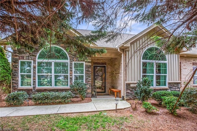 entrance to property featuring stone siding and roof with shingles