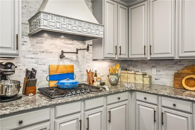 kitchen featuring tasteful backsplash, custom range hood, stainless steel gas cooktop, and gray cabinetry