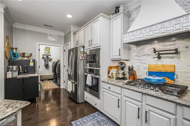 kitchen featuring visible vents, custom range hood, appliances with stainless steel finishes, ornamental molding, and washing machine and clothes dryer