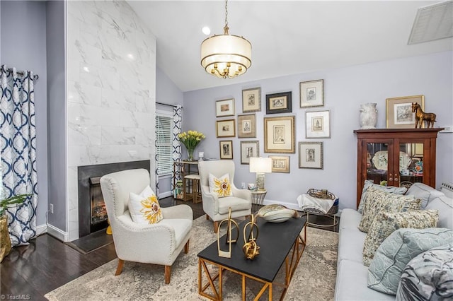 sitting room featuring baseboards, visible vents, lofted ceiling, wood finished floors, and a high end fireplace