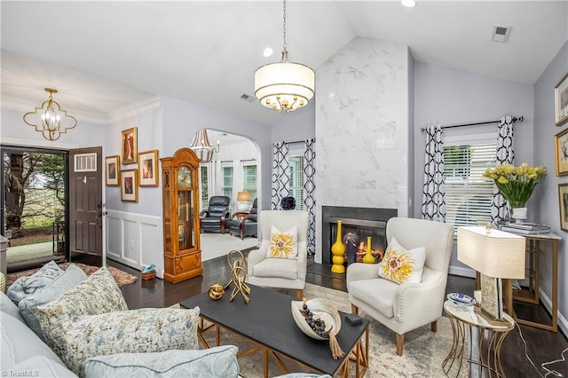 living room featuring lofted ceiling, a notable chandelier, a premium fireplace, visible vents, and wainscoting