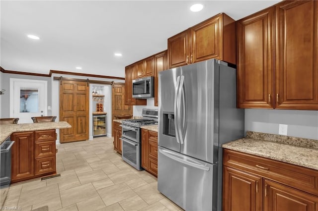 kitchen featuring appliances with stainless steel finishes, a barn door, recessed lighting, brown cabinetry, and ornamental molding