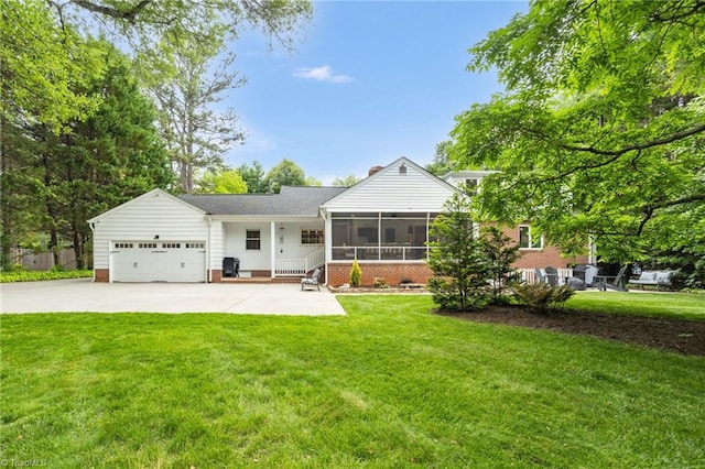 rear view of property featuring a lawn, an attached garage, a sunroom, and driveway