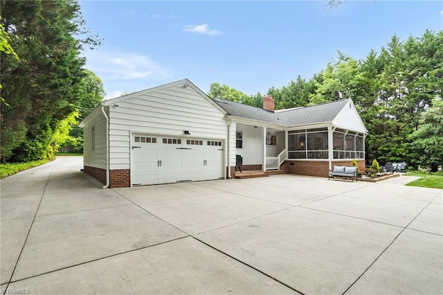 view of front of house featuring a sunroom, a chimney, an attached garage, concrete driveway, and brick siding