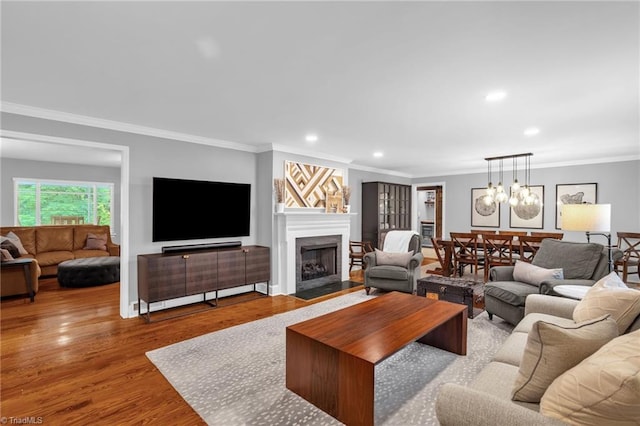 living room featuring wood finished floors, recessed lighting, ornamental molding, a fireplace with flush hearth, and a chandelier