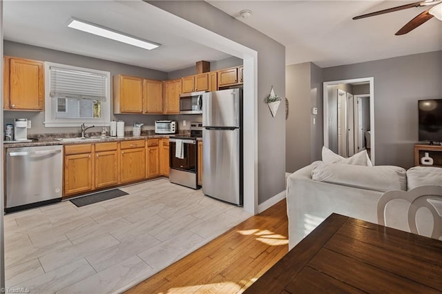 kitchen with light wood-type flooring, appliances with stainless steel finishes, ceiling fan, and sink