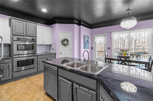 kitchen with gray cabinetry, stainless steel appliances, a sink, dark countertops, and crown molding