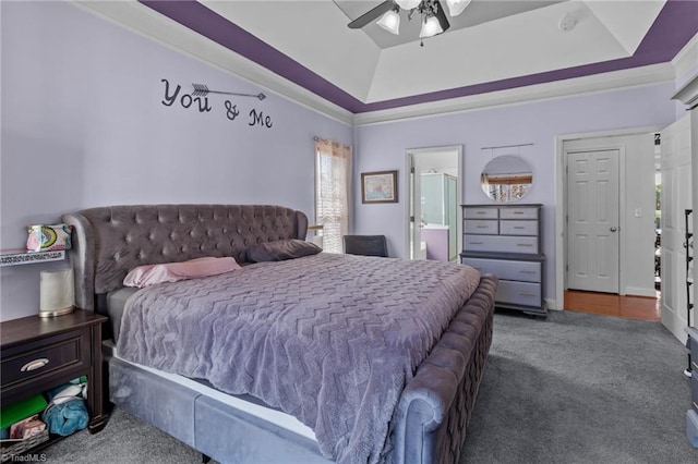 bedroom featuring ceiling fan, a tray ceiling, dark colored carpet, and connected bathroom