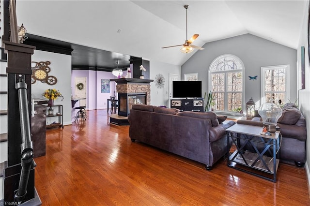 living area featuring baseboards, a ceiling fan, wood finished floors, vaulted ceiling, and a fireplace