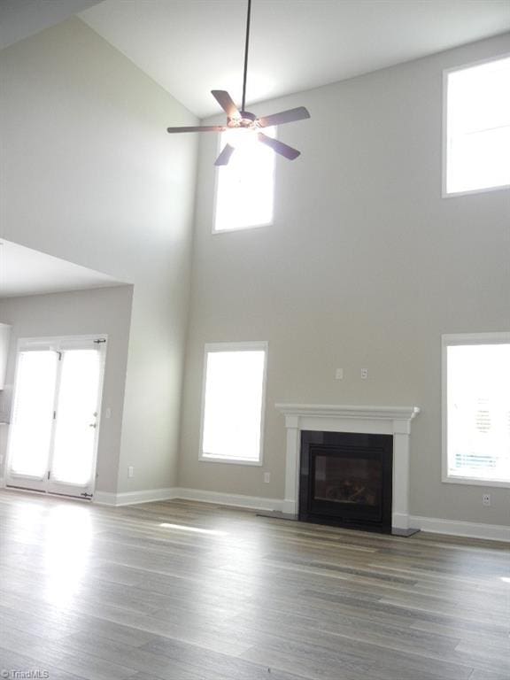 715 Cannonade Dr, Whitsett, NC 27377 - unfurnished living room featuring high vaulted ceiling, ceiling fan, wood finished floors, a glass covered fireplace, and healthy amount of natural light