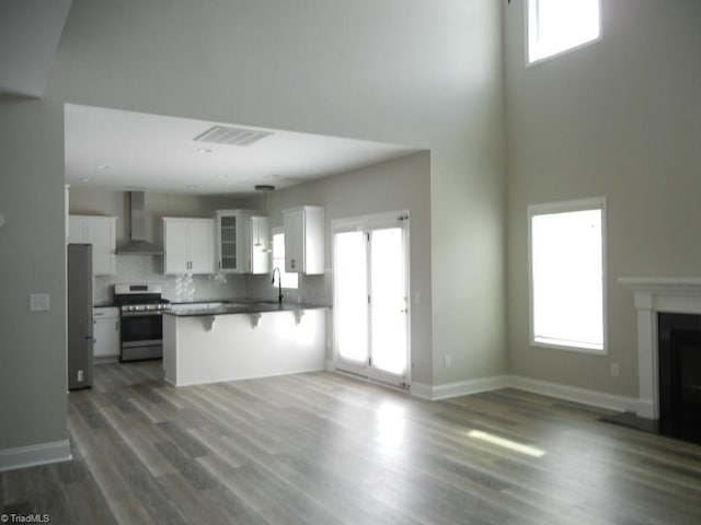 715 Cannonade Dr, Whitsett, NC 27377 - kitchen featuring stainless steel appliances, wall chimney range hood, a breakfast bar area, white cabinets, and a peninsula