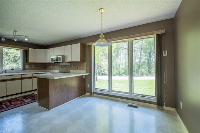 kitchen with stainless steel microwave, a textured ceiling, white cabinets, light countertops, and a peninsula