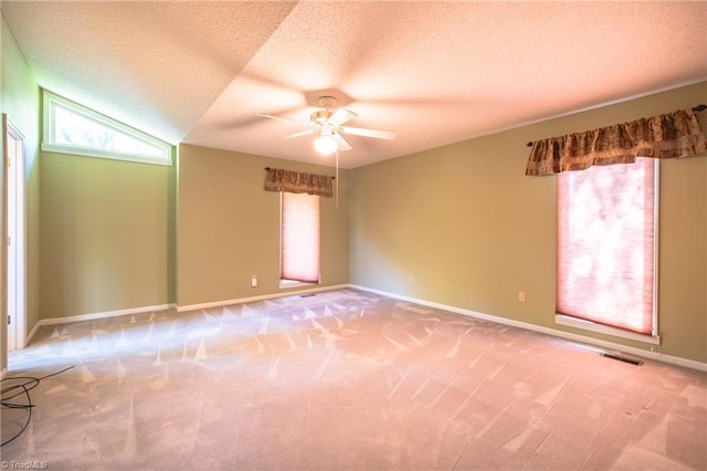 carpeted empty room with a ceiling fan, healthy amount of natural light, a textured ceiling, and baseboards