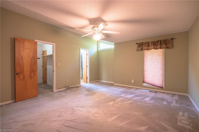 unfurnished bedroom with carpet flooring, a textured ceiling, a spacious closet, ceiling fan, and baseboards