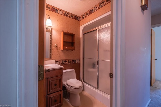 bathroom featuring wallpapered walls, a shower with shower door, toilet, vanity, and a textured ceiling