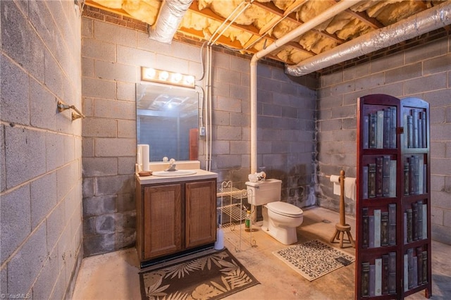 bathroom featuring unfinished concrete flooring, toilet, concrete block wall, and vanity
