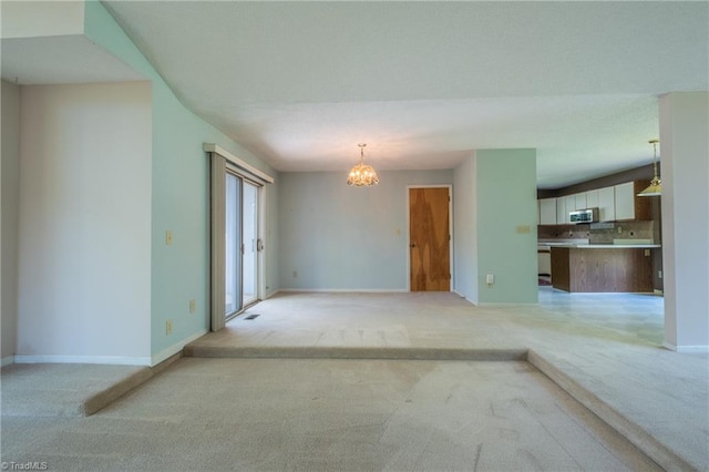 unfurnished living room with light carpet, a chandelier, and baseboards