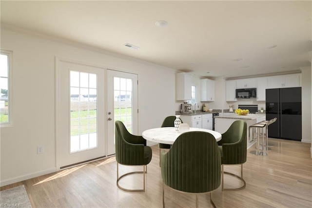 dining space featuring french doors, light hardwood / wood-style floors, crown molding, and sink