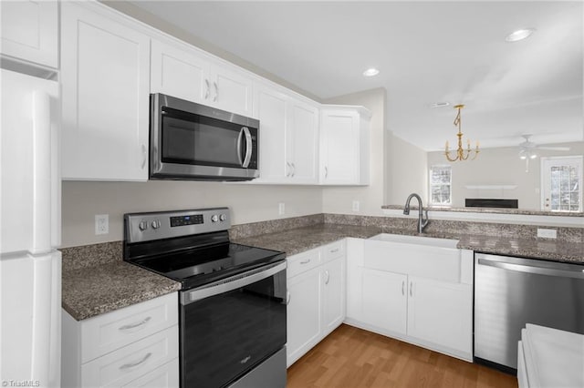 kitchen featuring appliances with stainless steel finishes, dark stone countertops, white cabinets, light hardwood / wood-style flooring, and sink