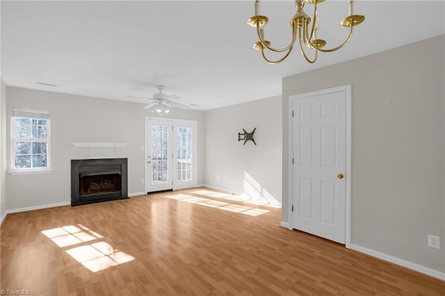 unfurnished living room with a wealth of natural light, ceiling fan with notable chandelier, and light hardwood / wood-style floors