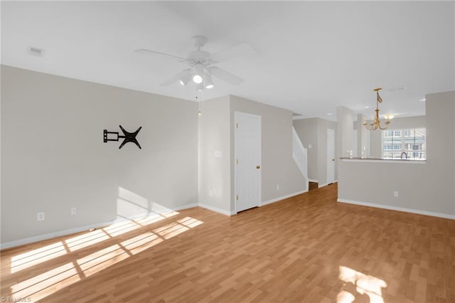 unfurnished living room with ceiling fan with notable chandelier and light hardwood / wood-style floors