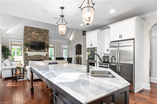 kitchen featuring appliances with stainless steel finishes, decorative light fixtures, a fireplace, white cabinetry, and an island with sink