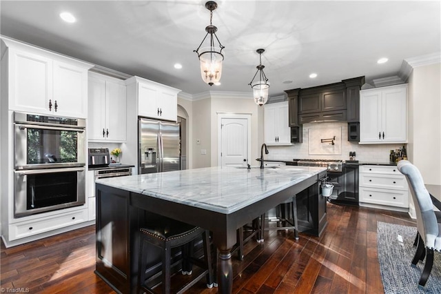 kitchen with appliances with stainless steel finishes, a breakfast bar, a large island with sink, decorative light fixtures, and white cabinetry