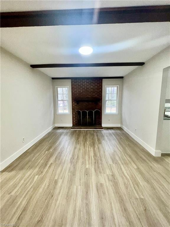 unfurnished living room featuring beam ceiling, a brick fireplace, and light wood-type flooring