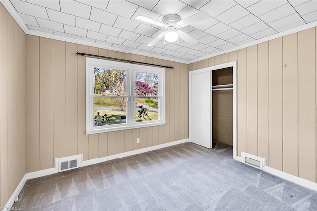 unfurnished bedroom featuring ceiling fan, crown molding, wood walls, carpet floors, and a closet