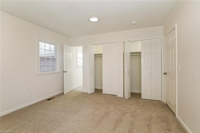 unfurnished bedroom with multiple closets and light colored carpet