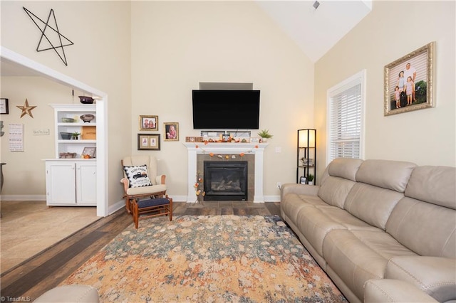 living room featuring a tile fireplace, high vaulted ceiling, and wood-type flooring