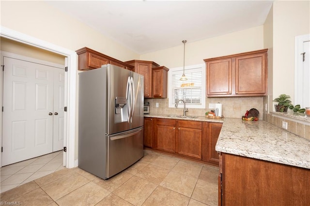 kitchen featuring backsplash, light stone counters, sink, pendant lighting, and stainless steel fridge with ice dispenser