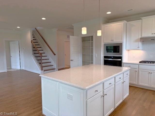 7607 Valhalla Way Lot 20, Greensboro, NC 27409 - kitchen with light wood finished floors, a center island, crown molding, white cabinetry, and appliances with stainless steel finishes