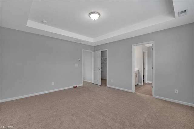 unfurnished bedroom featuring a closet, a spacious closet, ensuite bathroom, a tray ceiling, and light colored carpet