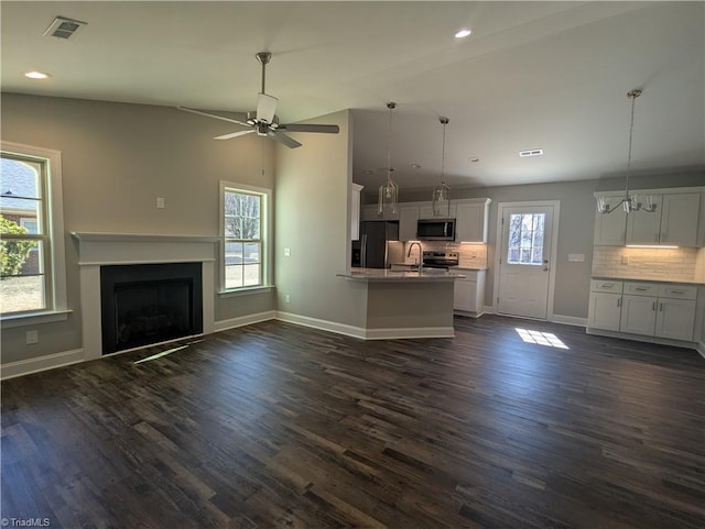 unfurnished living room featuring visible vents, dark wood-style flooring, baseboards, and a sink