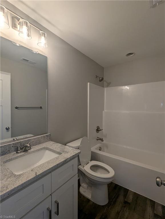 bathroom featuring visible vents, tub / shower combination, toilet, wood finished floors, and vanity