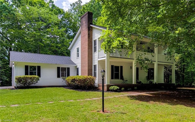 view of front facade featuring a chimney, a balcony, and a front yard