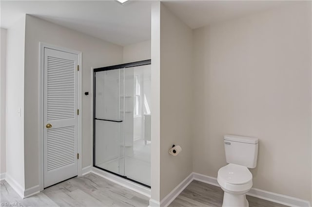 full bath featuring wood finished floors, a shower stall, toilet, and baseboards