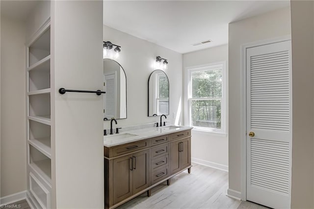 bathroom featuring wood finished floors, double vanity, baseboards, and a closet