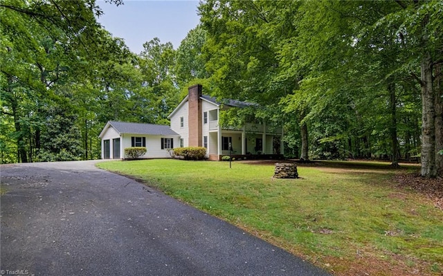 view of front of house featuring driveway, a chimney, a front yard, and a garage