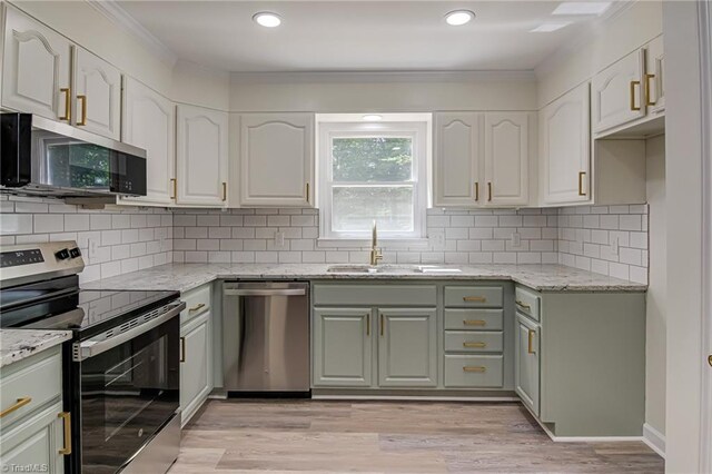 kitchen featuring appliances with stainless steel finishes, light stone counters, a sink, ornamental molding, and light wood-type flooring